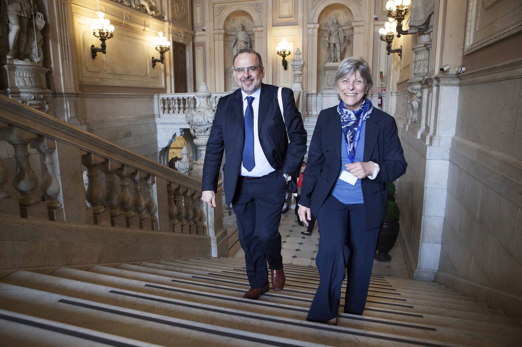 Man and woman smiling and walking up the stairs of a museum.  Luca Jahier, president of the European Economic and Social Committee at the Royal Museums, Turin © Image: Daniele Bottallo