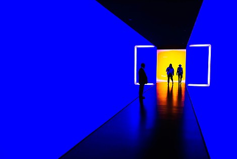 Three people walk through a light installation. They walk from a room lit in yellow into a blue tunnel.   © Image: Werner du Plessis