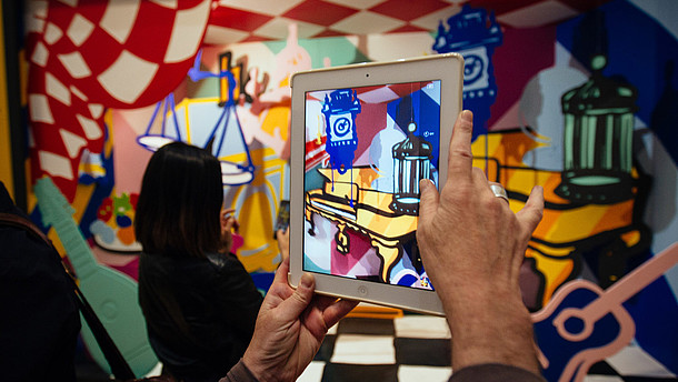 In this photograph a person takes a photo of a colourful and abstract installation using a tablet. The photo shows only their hands.  © Image: Courtesy Pimlico Project
