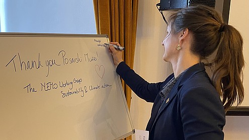 Person with hair tied up is seen from the side as she writes "thank you The NEMO Working Group Sustainability and Climate Action" on a white board.   