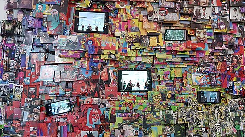 Part of a wall art work of a paper collage and smartphones and tablets that record and live show the people looking at the wall.   