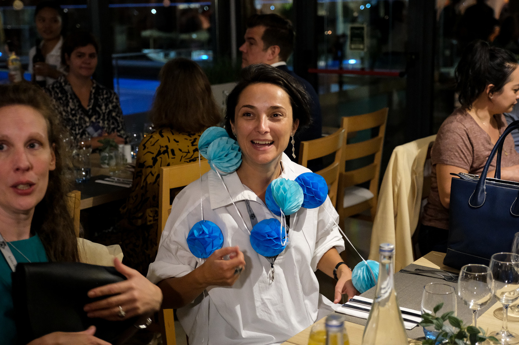 People are sitting on a restaurant table. One of them has a blue garland around their neck and is smiling.  © Image: Jorge Gomes