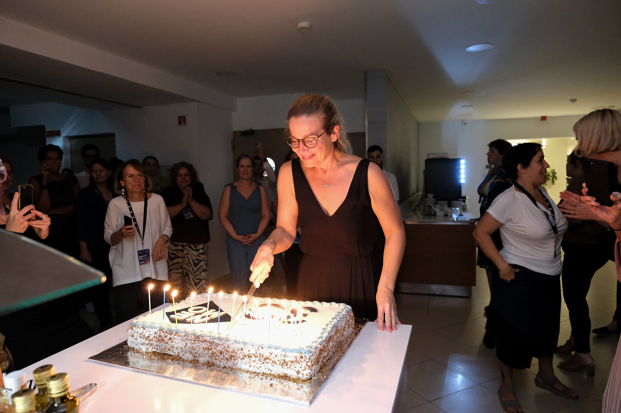 A person is cutting a cake lit by candles. Around them people are watching and taking photographs.  © Image: Jorge Gomes