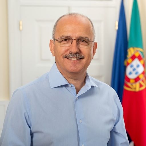  Half-length portrait of a smiling person. A flags of the EU and Portugal are in the background.