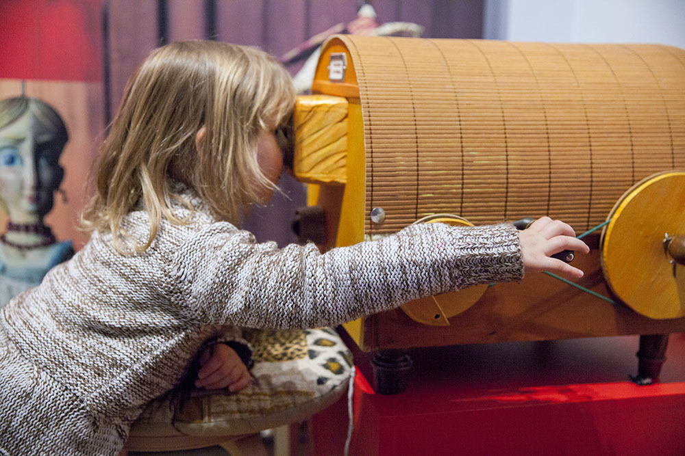© Image: R.Kodera © Image: R.Kodera A young child looks into a wooden construction with wheels. With one hand they turn a winder.