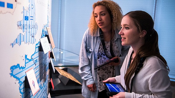 Two women use a tablet to engage with an interactive art piece.
