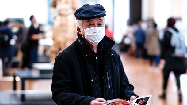 Man wearing face mask is walking through an exhibition space while flipping through pamphlet.  © Image: Lucrezia Carnelos