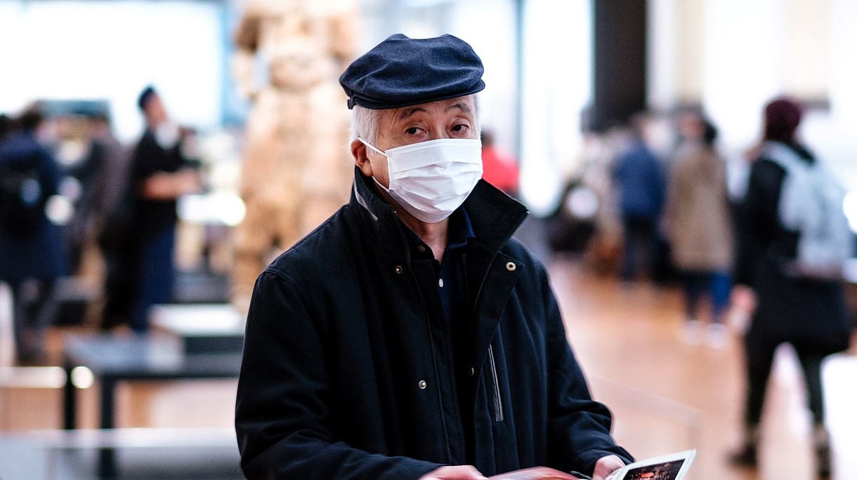 © Image: Lucrezia Carnelos Man wearing face mask is walking through an exhibition space while flipping through pamphlet.