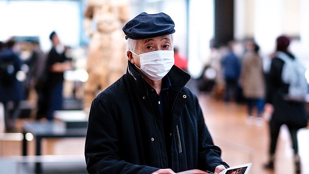  Man wearing face mask is walking through an exhibition space while flipping through pamphlet.