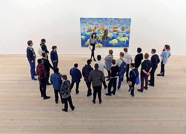 A group of people stand in front of a modern painting together with a museum educator. The image is photographed from bird perspective.