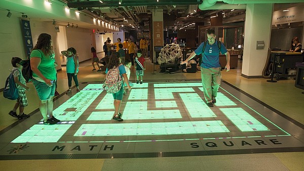 A group of children and adults interact with a digital projection on the floor.