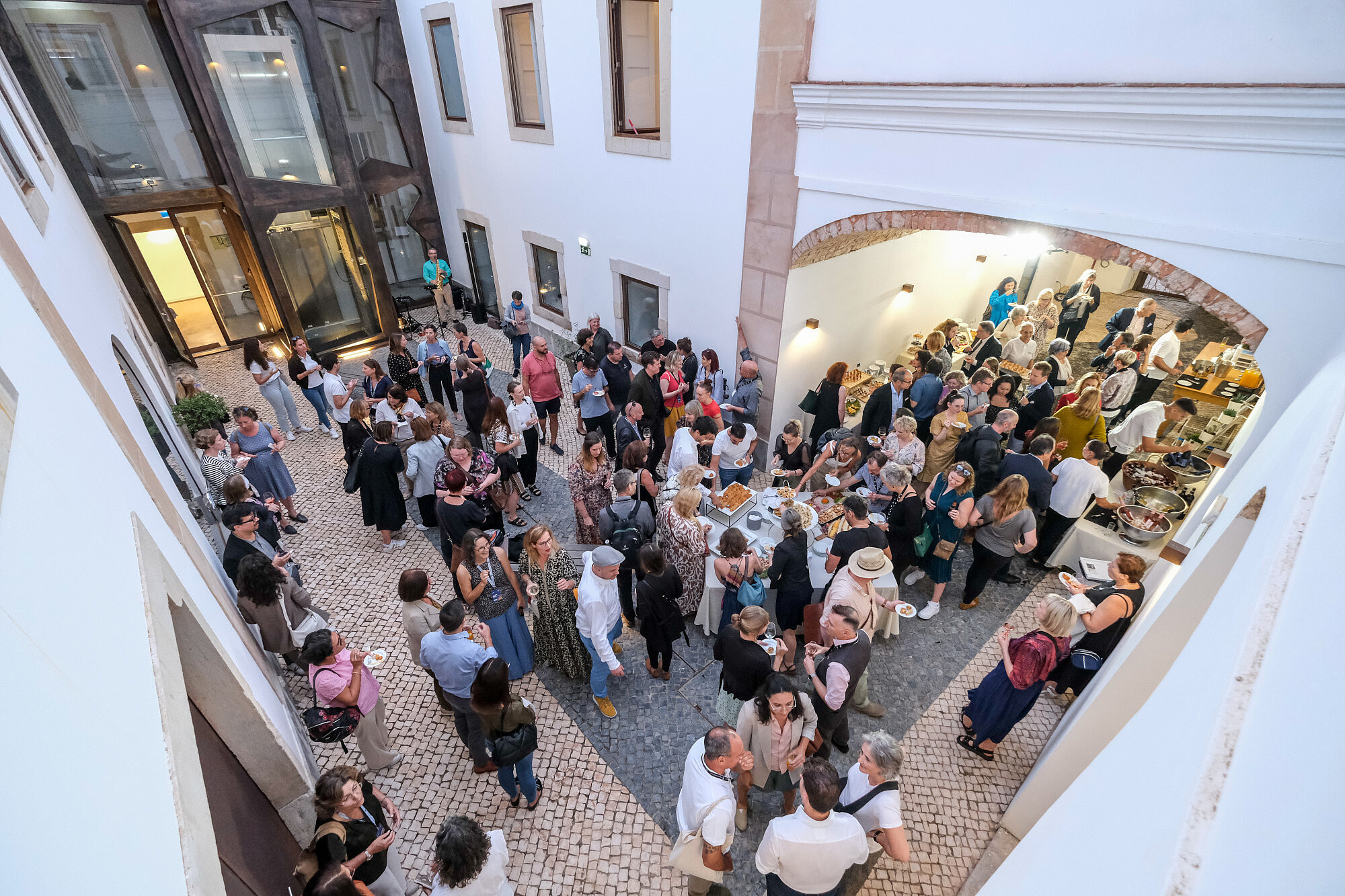 © Image: Jorge Gomes Photo taken from bird perspective of a large group of people standing inside a courtyard. Some people are standing by a buffet, others are socialising or eating. © Image: Jorge Gomes