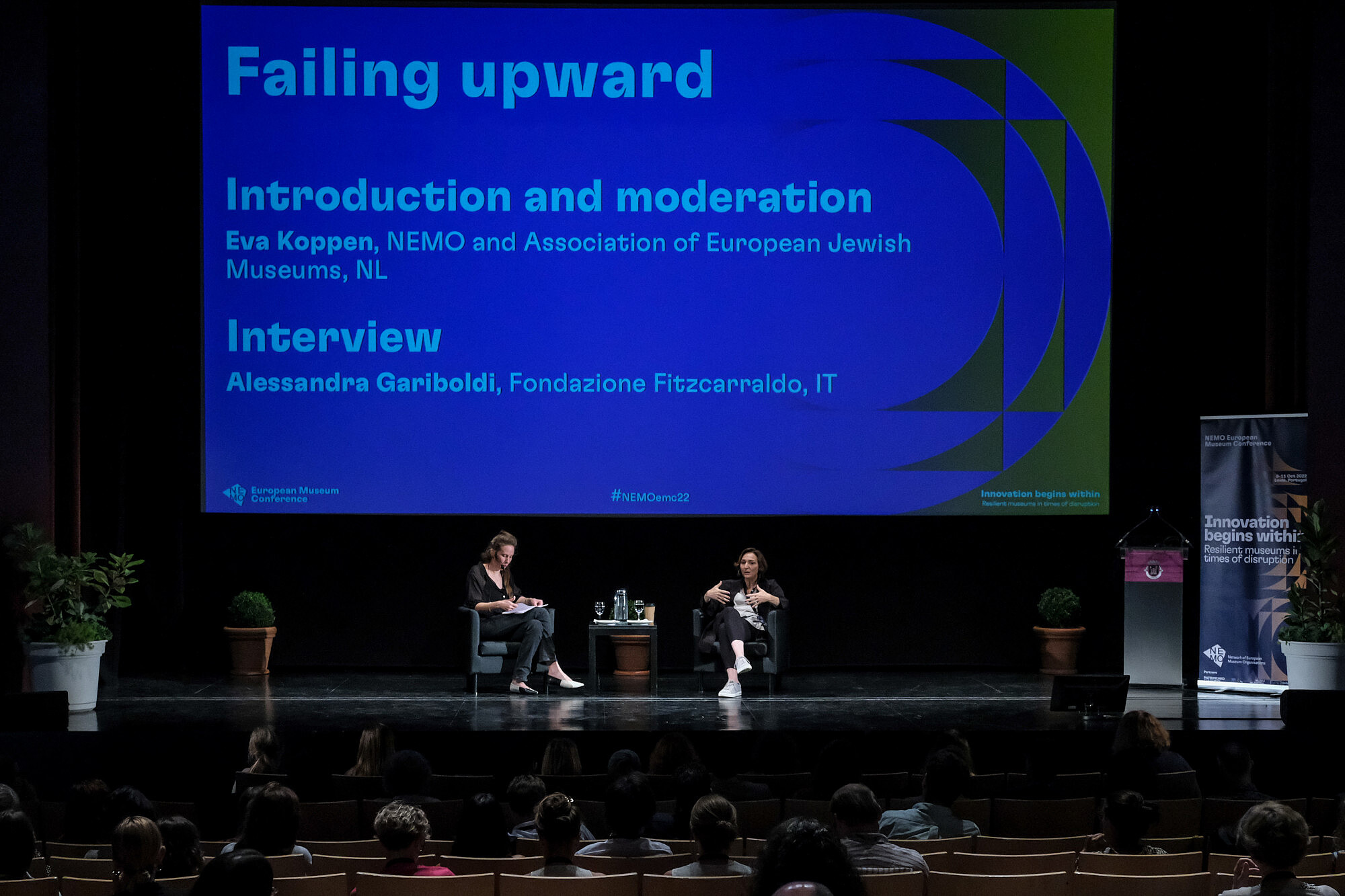 © Image: Jorge Gomes Two people sit on a stage. On of them is gesturing and talking to an audience. © Image: Jorge Gomes
