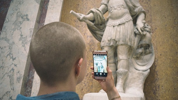  A person, shown from behind, is taking a picture of a sculpture with their smartphone.