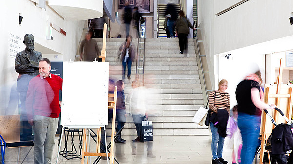 Several people moving in a staircase during a painting workshop at a museum. They are blurry due to the long exposure of the photograph.