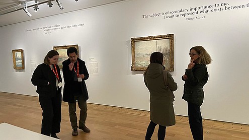 Four people are walking through an exhibition hall in pairs of two. Both pairs appear to be deep in conversation.   