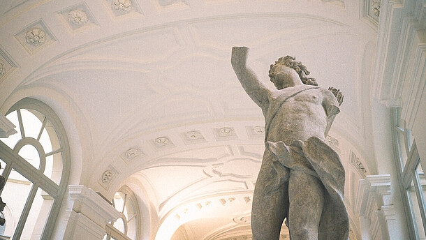 A classical sculpture of a person is shown from below. Their arms are missing.