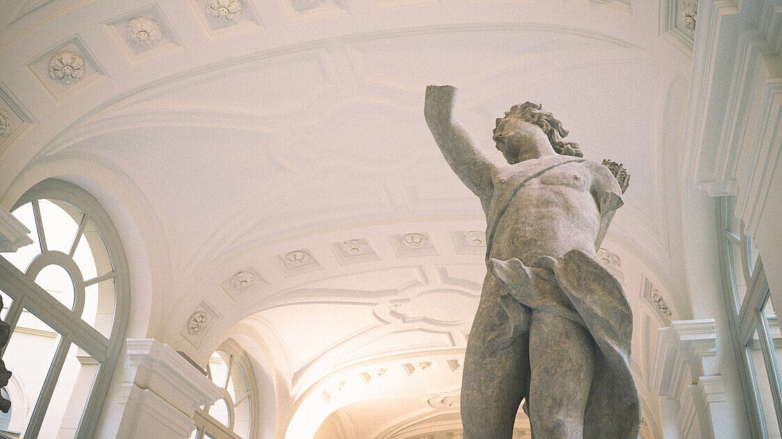A classical sculpture of a person is shown from below. Their arms are missing.