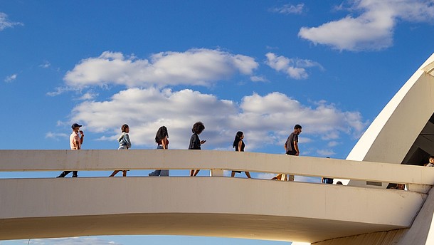  Six people walk behind each other over a bridge. 