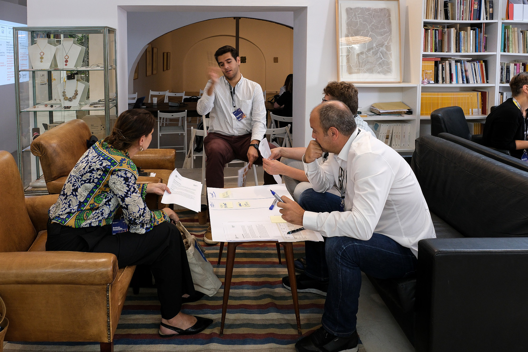 Four people are sitting around a small table. On the table is a large piece of paper with notes. One person is talking an gesturing with their arms, while two of the others are looking at them.  © Image: Jorge Gomes