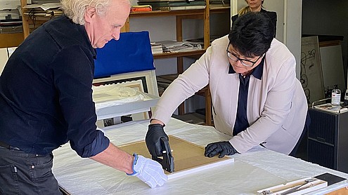 Sabine Verheyen leans forward to staple the back of picture frame with the help of a person holing the frame together.   
