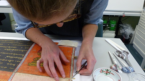 Photo of someone leaning over to get closer to an ancient piece of paper to do some restoration work. 