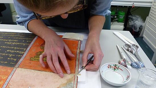 Photo of someone leaning over to get closer to an ancient piece of paper to do some restoration work. 