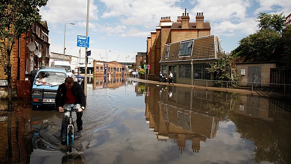 A person on a bicycle is riding through a flooded street in an urban setting.