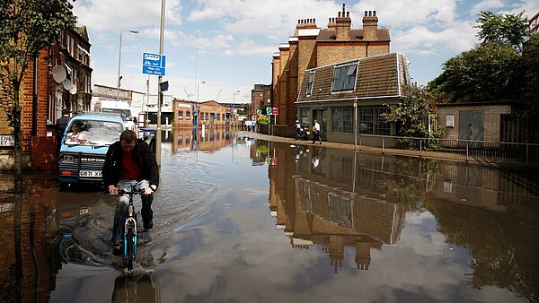 A person on a bicycle is riding through a flooded street in an urban setting.