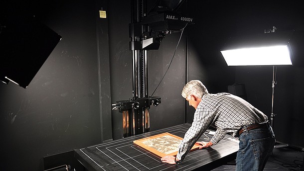  Man leaning over a table positioning a picture that he is photographing in order to digitalize it