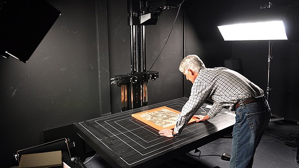  Man leaning over a table positioning a picture that he is photographing in order to digitalize it
