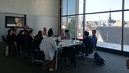 Group of people are sitting around a table with their backs to the photographer listening to a presentation.