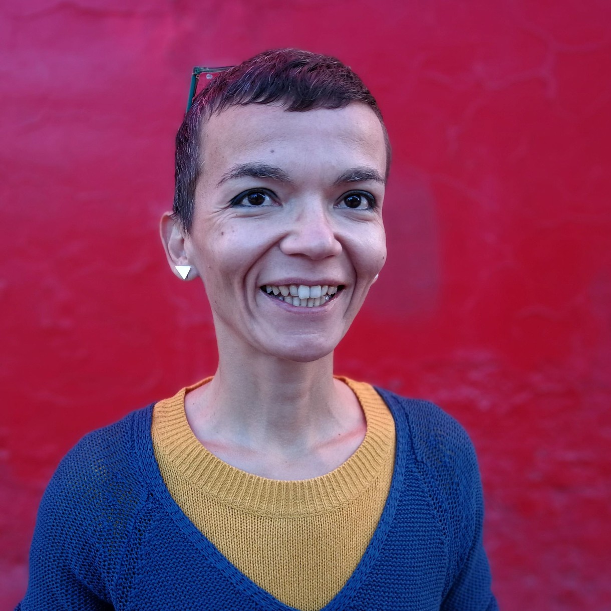  Portrait of a person standing in front of a red wall and smiling into the camera.