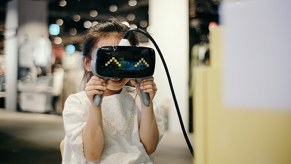 A girl is using a pair of VR goggles in a gallery space. The child is smiling and the goggles mirror the smile with happy eyes animation.