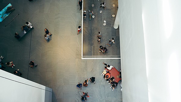 Photo taken from bird perspective of an exhibition space. People are walking and looking at art. 
