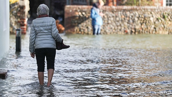 A person, photographed from the back, is walking barefoot through a flooded street. 