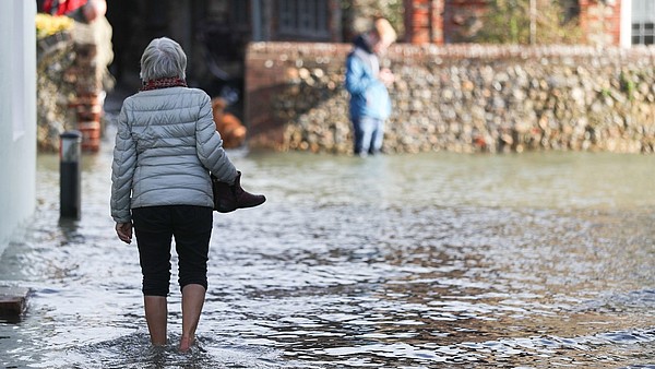 A person, photographed from the back, is walking barefoot through a flooded street. 