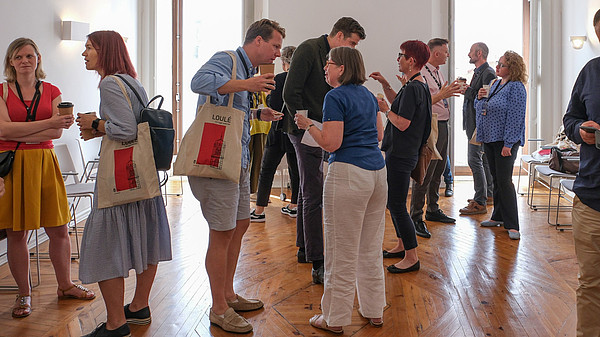 Numerous people are standing in groups and talking to each other.