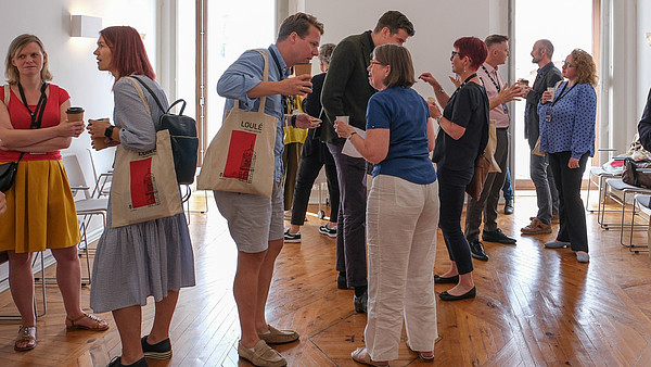 Numerous people are standing in groups and talking to each other.