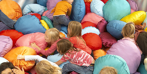 Children are crawling over numerous brightly coloured cushions. 