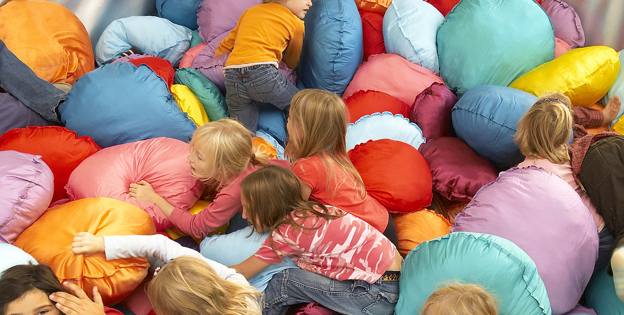  Children are crawling over numerous brightly coloured cushions. 