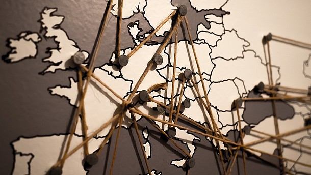  This photographs shows a map of europe. On the map, nails are attached, which are connected by a piece of string.