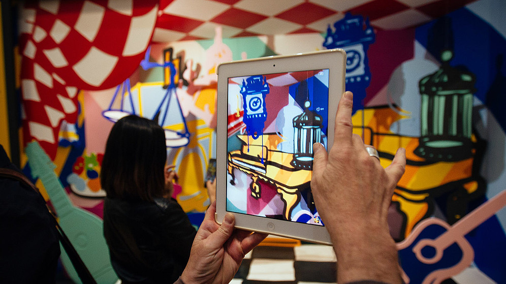 In this photograph a person takes a photo of a colourful and abstract installation using a tablet. The photo shows only their hands.  © Image: Courtesy Pimlico Project