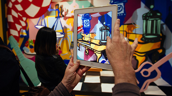 In this photograph a person takes a photo of a colourful and abstract installation using a tablet. The photo shows only their hands.