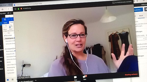 Photograph taken of a computer screen. On the screen is a video of a person talking in a zoom meeting.