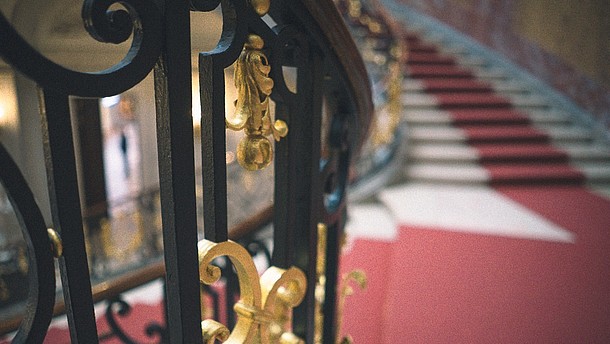  Detail of an iron handrail with view of the stairwell in the back.