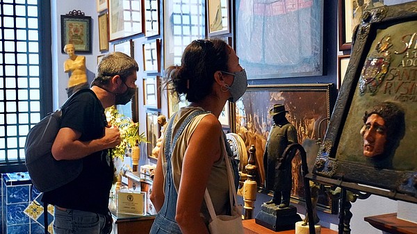 Two people wearing face masks are looking at art hanging on the wall.
