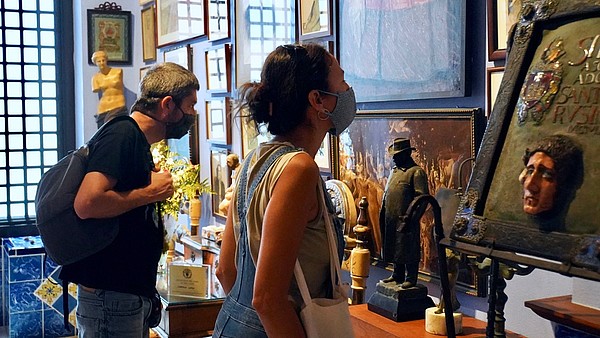 Two people wearing face masks are looking at art hanging on the wall.