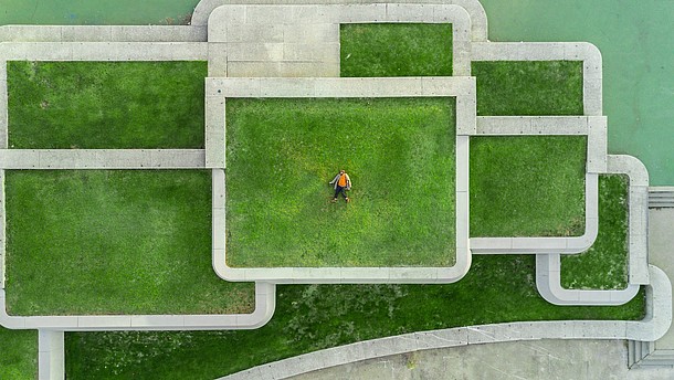  Aerial view of a modern architectural structure made out of concrete rectangles. Inside the rectangles grass is growing and a person is laying down in one of them. 