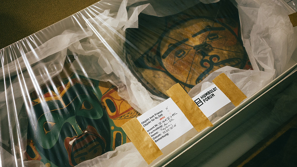 This photo shows two ancient art objects packaged inside a box with foil on top. On the foil is a sticker of the "Humboldt Forum" as well as an inventory sticker.  © Berlin State Museums, Image: Daniel Hofer